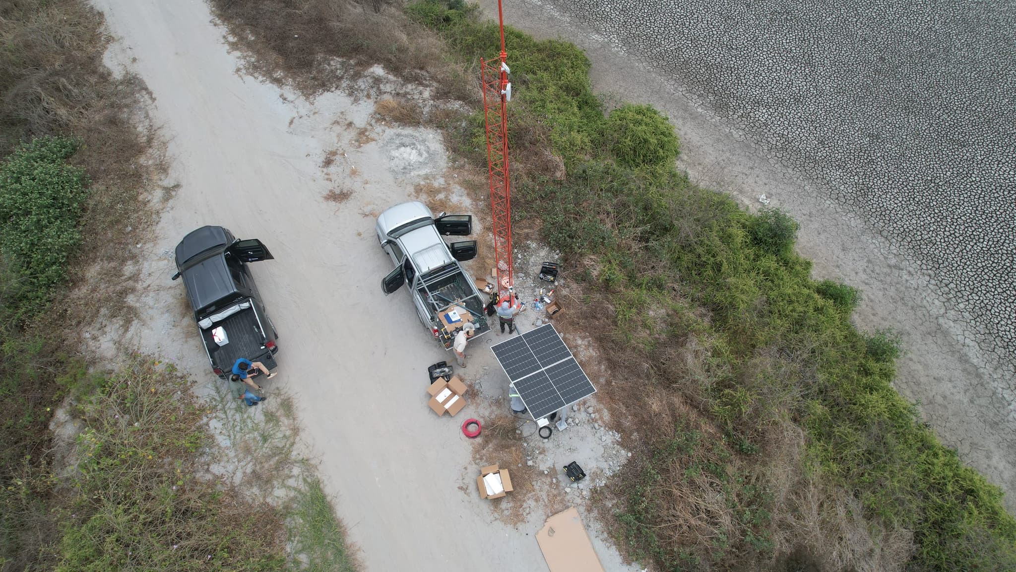 Cuadrilla de INVOCE montando torre arriostrada con antenas y arreglo fotovoltaico sobre el dique de una camaronera.